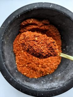 a bowl filled with spices and a spoon full of ground chili powder on top of it