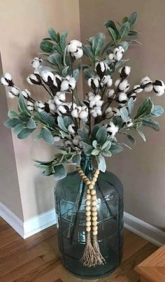 a vase filled with cotton and greenery on top of a wooden floor