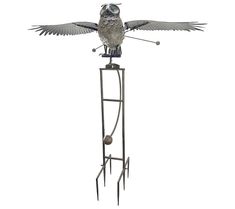 an owl statue on top of a metal pole with its wings spread out and two balls in the air