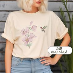 The unisex soft-style floral hummingbird t-shirt is not only beautiful, it's extra soft and comfy. It is the perfect spring or summer T-shirt that's dressy casual. It also makes a wonderful birthday gift or Mother's Day. Available in five pretty color choices: Natural, Heather Royal, Heather Indigo, Sapphire or White. In sizes S-3X Made with 100% ring-spun cotton. Fabric blends: Heather colors - 35% ring-spun cotton, 65% polyester;  Sport Grey and Antique colors - 90% cotton, 10% polyester, Grap Hummingbird Inspired Outfit, Summer Crew Neck T-shirt With Bird Print, Cute Butterfly Print T-shirt For Spring, Womens Bird Shirt, Casual Summer T-shirt With Bird Print, Casual Crew Neck T-shirt With Bird Print, Spring Botanical Flower T-shirt, Floral Tee, Spring Tops