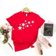 a red shirt with white stars on it next to pink flowers and sunglasses, a pair of sneakers