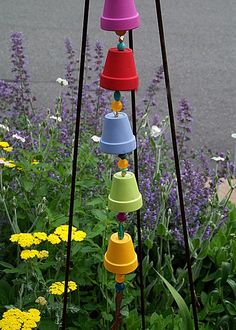 a bunch of colorful bells hanging from poles in front of some flowers and plants on the side of the road