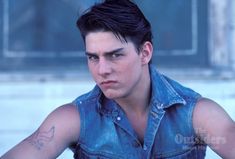 a man with tattoos on his arm wearing a denim vest and looking at the camera