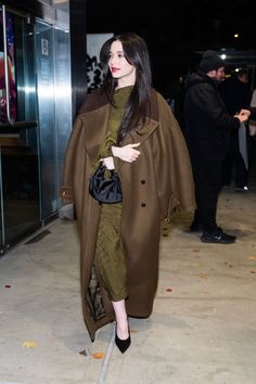 a woman is walking down the street wearing a brown coat and green dress with black heels