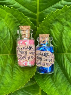 two small bottles filled with colorful confetti on top of a green leaf covered ground