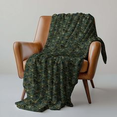 a chair with a blanket on top of it next to a brown leather arm chair