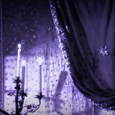 two candles are lit in front of a window covered with curtains and snowflakes