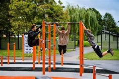 two young men are playing in the park on an outdoor gym equipment set with orange bars