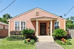 a small pink house sitting on the corner of a street with trees and bushes in front of it