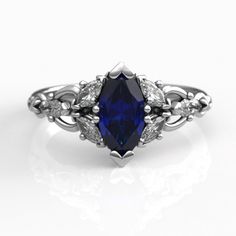 a blue sapphire and diamond ring with leaves on the sides, set in white gold