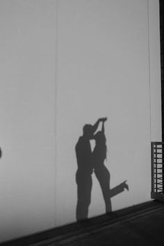 two people standing next to each other in front of a wall with their shadow on it