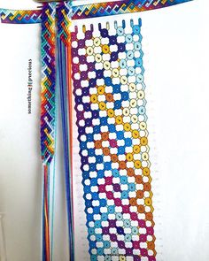 a cross stitch bookmark hanging on a white wall with two ribbons attached to it