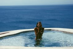 a woman sitting in the middle of a hot tub next to the ocean with her hands on her face