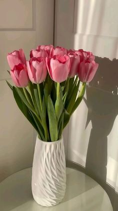 a white vase filled with pink flowers on top of a table