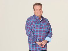 a man in a blue and red checkered shirt is standing with his hands on his hips