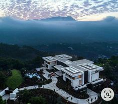 an aerial view of a house in the middle of trees and mountains with clouds overhead