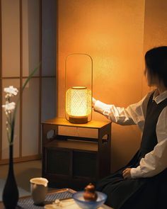 a woman sitting in front of a table with a lamp on it