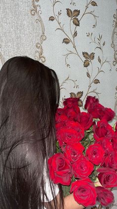 a woman holding a bunch of red roses in her hand and looking at the wall