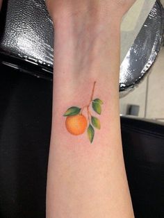 an orange tattoo on the wrist of a woman's left arm, with green leaves