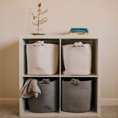 four baskets are stacked on top of each other in front of a wall with a small tree