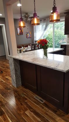 a kitchen with wooden floors and lights hanging from the ceiling over the island counter top