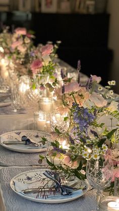 a long table is set with candles and flowers in vases, plates and glassware