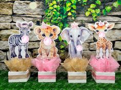 three little giraffes and two baby elephants are sitting in small boxes on the grass