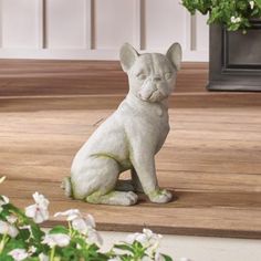 a white dog statue sitting on top of a wooden floor next to a potted plant