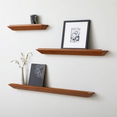 two wooden shelves on the wall, one with a vase and an empty photo frame