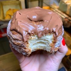 a person holding a chocolate covered doughnut in their hand, with the frosting on it