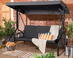 a black swing bed with orange and white pillows on it in front of a brick wall