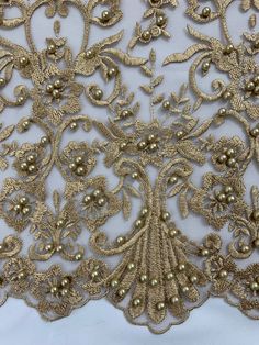 gold beaded lace with pearls and flowers on white fabric, close - up view