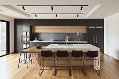 a large kitchen with wooden floors and white counter tops, along with black bar stools