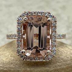 an engagement ring with a large pink diamond surrounded by white and brown diamonds, on top of a rock