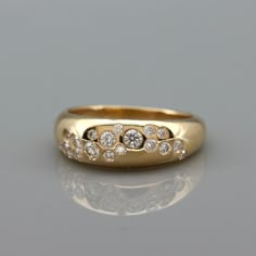 a yellow gold ring with five diamonds on the outside and in the middle, sitting on a reflective surface