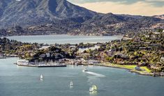 sailboats are sailing in the water near a city and mountain range, with mountains in the background