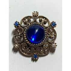 Vintage Gold Tone Filigree Brooch Blue Stones and Pearls. In great vintage condition. Pretty gold tone filigree setting is adorned with blue stones and pearls and a large blue center stone. Pin mechanism is in good working order. Measures approximately 1.25 x 1.25 x .5 inches. PINGUNK252 Antique Blue Jewelry With Brooch, Blue Cabochon Brooch For Formal Occasions, Blue Victorian Brooch For Formal Occasions, Formal Blue Cabochon Brooch, Victorian Blue Brooch For Formal Occasions, Blue Victorian Brooches For Formal Occasions, Elegant Blue Jeweled Brooches, Vintage Blue Cabochon Jewelry, Vintage Sapphire Brooch Jewelry