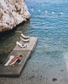 a man laying on a concrete dock next to the ocean