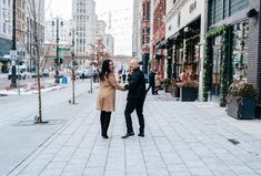 a man and woman are standing on the street holding hands while talking to each other