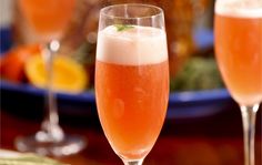 two wine glasses filled with pink liquid on top of a table next to a plate of food