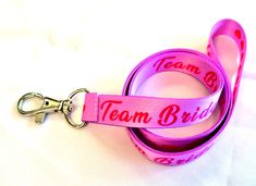 "TEAM BRIDE pretty printed neck strap lanyard (non-detachable clasp, 15mm width). From our range of novelty neck strap lanyards. Pink on pink TEAM BRIDE image on both sides of a quality lanyard. Also available with a safety breakaway. High quality UK printed ID holder lanyards, printed on both sides, fitted with a metal clip, to be worn around the neck to carry ID, access cards, keys etc. Product code : H-317 Hand made in the UK Size: 94cms (36\") Width : 15mm (0.59\") Silver metal clip *  Great quality and value *  Beautifully coloured, bright vivid sublimation print *  Lightweight *  Smooth polyester fabric remains comfortable to wear *  Long lasting metal trigger clip UK manufacturer and seller All prices include free UK post & packing All lanyards are individually packed Available in 3 Adjustable Personalized Pink Lanyard, Rose Image, Personalized Lanyards, Custom Lanyards, Key Lanyard, Uk Post, Team Bride, Id Holder, Neck Strap