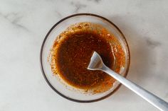 a glass bowl filled with sauce on top of a white marble counter topped with a metal spoon