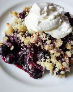 a white plate topped with blueberry crumble and whipped cream on top of it