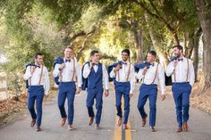 a group of men walking down a road wearing blue suits and bow ties, with trees in the background