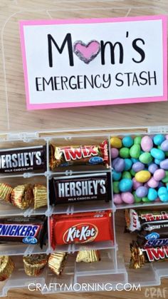 a plastic container filled with candy and candies on top of a wooden table next to a sign that says mom's emergency stash