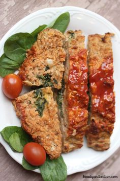 meatloaf with tomato sauce and spinach leaves on a white plate next to cherry tomatoes