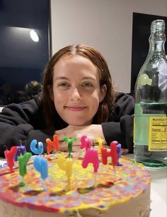 a woman sitting in front of a cake with candles on it and a bottle behind her