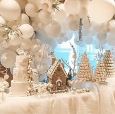 a table topped with lots of white balloons and cake covered in frosted icing