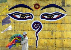 a man holding a colorful umbrella in front of a wall painted with an image of the face of buddha