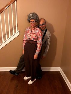 an older couple standing next to each other in front of a stair case and wooden floor